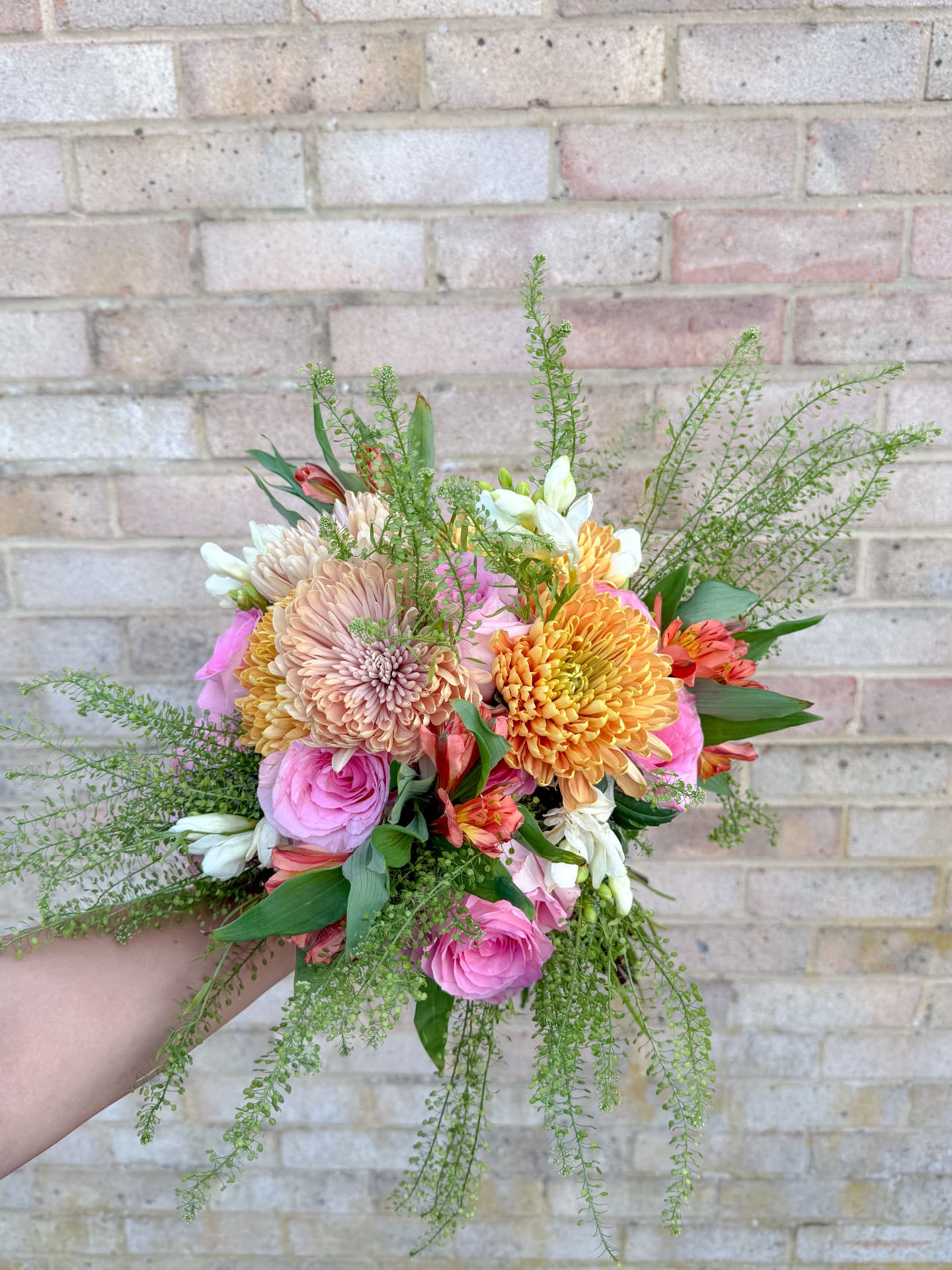 Hand-tied bridal bouquet of pink roses, peach chrysanthemums and trailing greenery