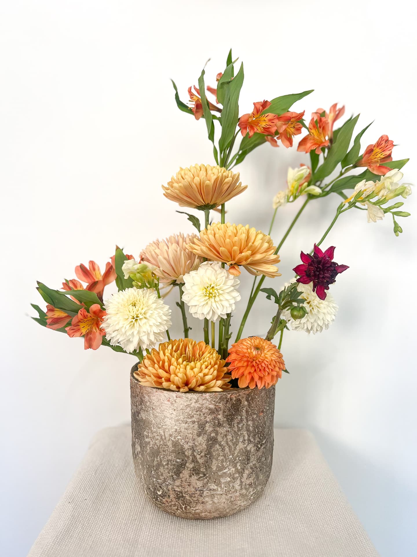 Peach and cream dahlias and chrysanthemums in a stone pot